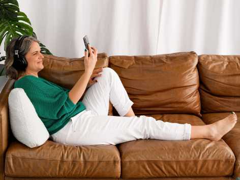 Laura McRae sitting on sofa listening to a podcast